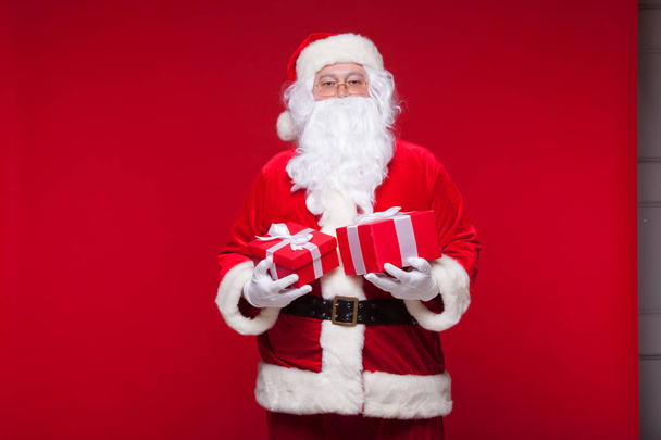 Christmas. Photo Santa Claus giving xmas present and looking at camera, on a red background - Valokuva, kuva
