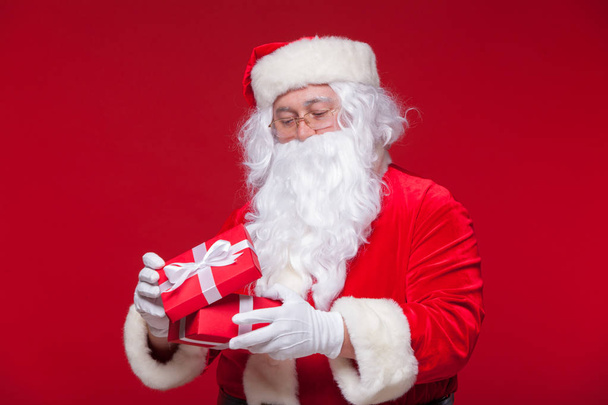 Christmas. Photo Santa Claus giving xmas present and looking at camera, on a red background - Fotografie, Obrázek