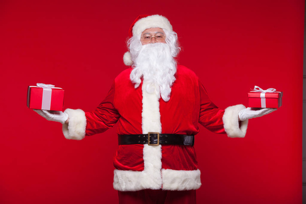 Christmas. Photo Santa Claus giving xmas present and looking at camera, on a red background - Foto, Bild