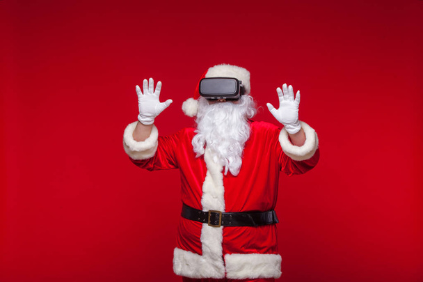 Santa Claus wearing virtual reality goggles, on a red background. Christmas - Fotoğraf, Görsel