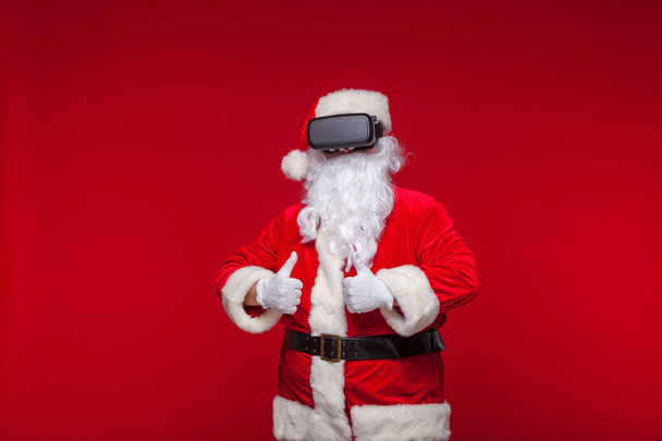 Santa Claus wearing virtual reality goggles, on a red background. Christmas - Photo, image