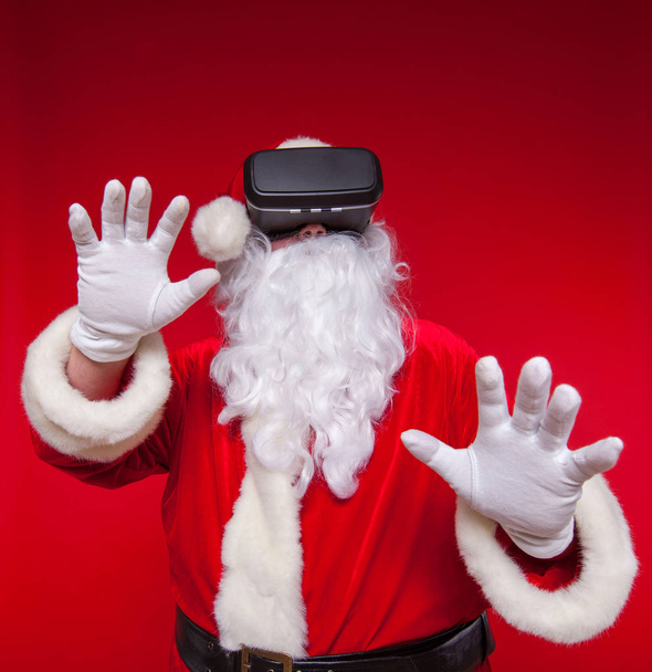Santa Claus wearing virtual reality goggles, on a red background. Christmas - 写真・画像
