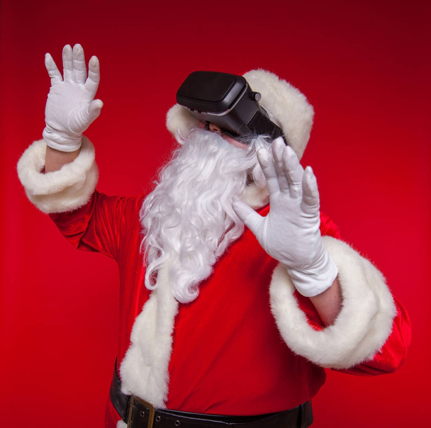 Santa Claus wearing virtual reality goggles, on a red background. Christmas - Zdjęcie, obraz