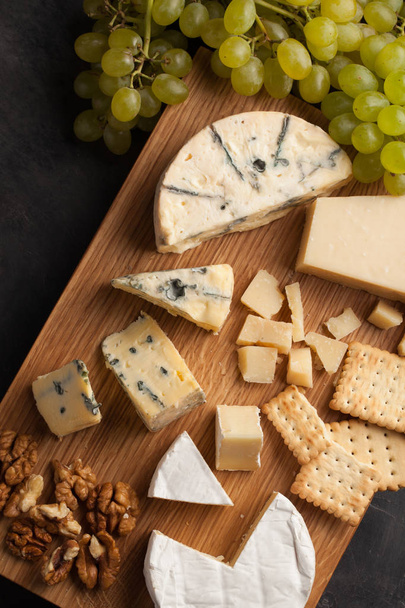 Kóstolása sajttál a fából készült lemez. Élelmiszer, a bor és romantikus, sajt delikátesz a sötét kő asztal. Szemközti nézet - Fotó, kép