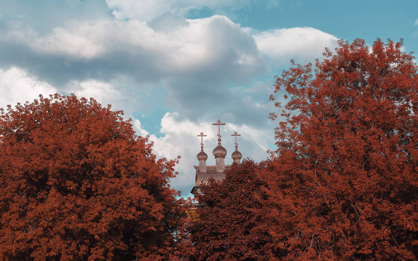 Iglesia de madera detrás de árboles rojos de otoño
 - Foto, imagen