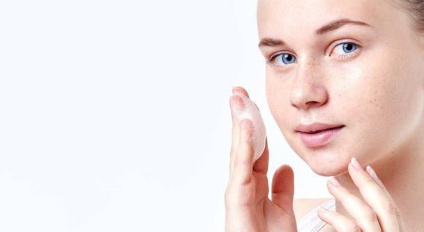 Teenager skincare. Smiling beautiful teen girl with freckles and blue eyes using foaming cleanser. Face washing concept isolated on white background. - Фото, изображение