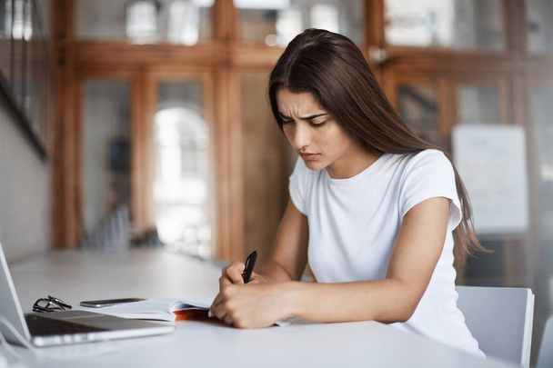 Une jeune femme concentrée qui écrit une lettre dans un carnet sans utiliser un ordinateur portable pour rassembler ses pensées
. - Photo, image