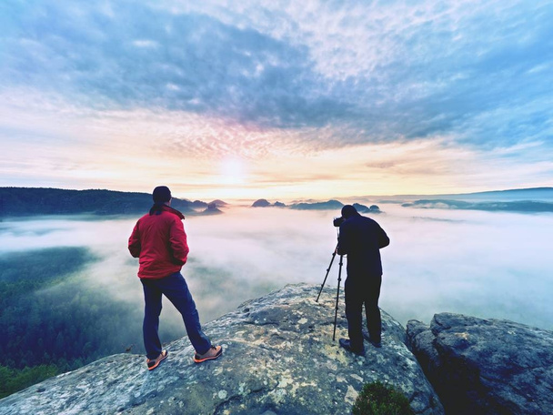 Fotografieren in freier Natur. Naturfotograf mit großer Kamera auf Stativ bleibt auf Gipfelfelsen. Muse anhören - Foto, Bild