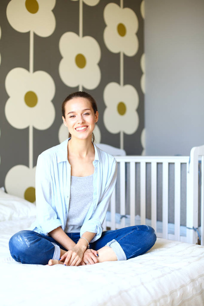 Young woman sitting on the bed near childrens cot. Young mom - Fotografie, Obrázek