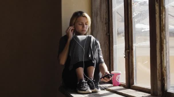 Tyttö näyttää hyvin surullinen kuunnellessaan musiikkia kuulokkeet ikkunan - Materiaali, video