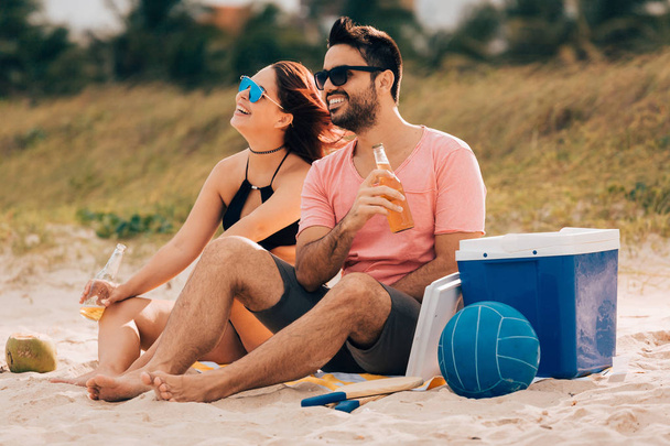 Couple drinking beer and having fun on the beach - Фото, изображение