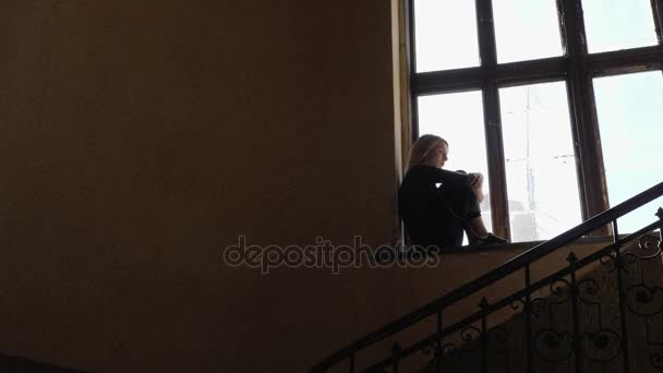 Sylwetka dziewczynki wygląda smutno podczas słuchania muzyki na słuchawkach przez okno - Materiał filmowy, wideo