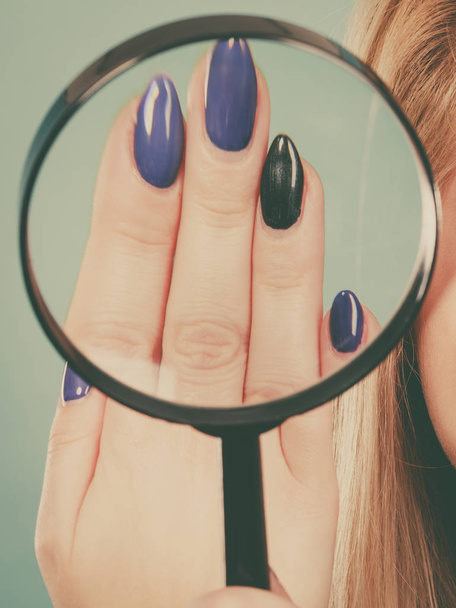 Woman looking at nails through magnifying glass - Foto, Imagen