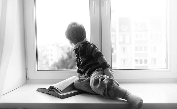 Der kleine Junge liest ein Buch. das Kind sitzt am Fenster a - Foto, Bild