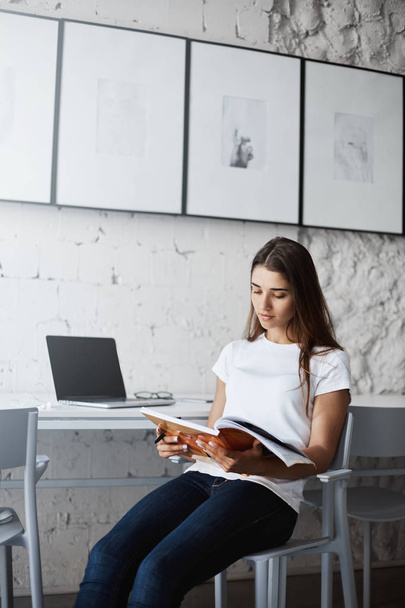 Mujer joven leyendo una revista relajante después de largas horas de trabajo en su computadora portátil
. - Foto, imagen