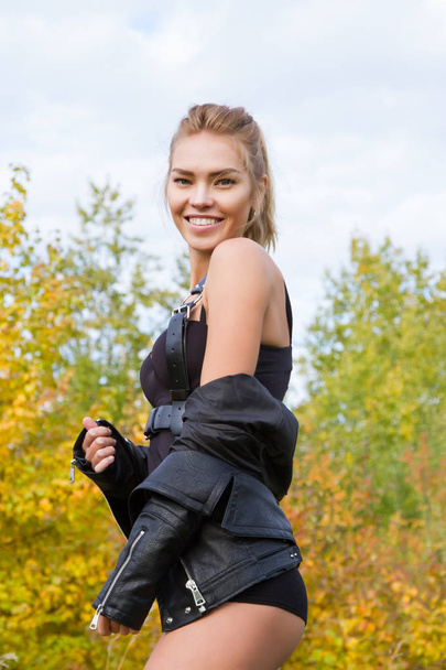 Menina sexy em uma jaqueta de couro e munição entre as folhas de outono
 - Foto, Imagem