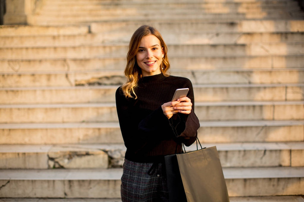 Mujer joven con bolsa de compras y teléfono móvil al aire libre
 - Foto, imagen