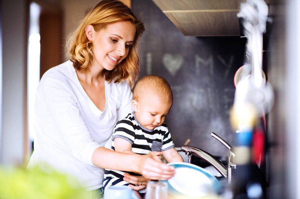 Young mother with a baby boy doing housework. - Foto, Bild