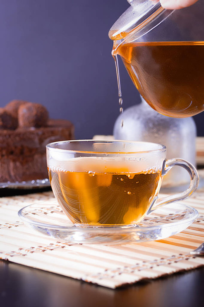 Öntés egy átlátszó üveg teáskanna tea egy átlátszó üveg pohár a csészealj - Fotó, kép