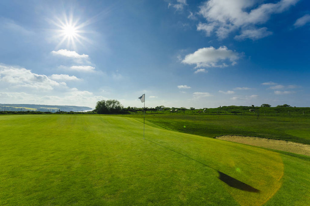 Vista di un campo da golf verde, buca e bandiera in una giornata luminosa e soleggiata. Sport, relax, svago e tempo libero. Paesaggio estivo con raggi di sole
 - Foto, immagini