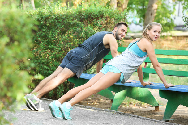 Young man and woman doing exercises in park - Photo, Image