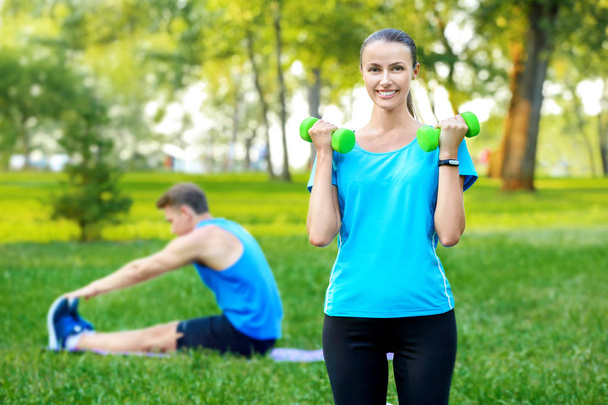 Young sporty couple doing exercises in green park - Φωτογραφία, εικόνα