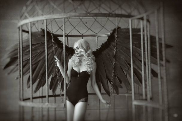 blond woman with black wings in a cage. Angel, mysticism - Foto, afbeelding