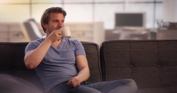 Young man drinking coffee on his couch - Imágenes, Vídeo