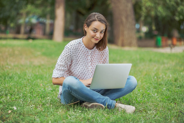Νεαρή γυναίκα με φορητό υπολογιστή κάθεται στο πράσινο γρασίδι - Φωτογραφία, εικόνα