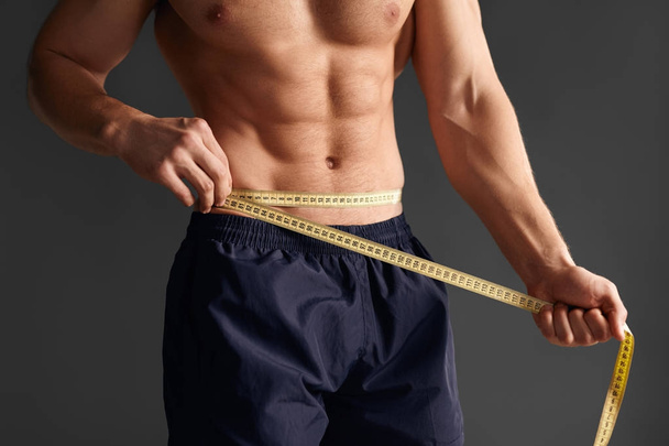 Crop sportsman measuring waist - Foto, afbeelding