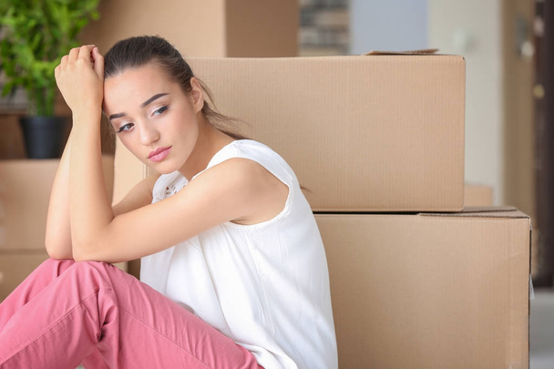 Unavený mladá žena sedící na podlaze v jejím novém bytě poblíž stěhovací krabice - Fotografie, Obrázek
