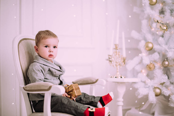 Vrolijk baby jongetje spelen met geschenken en presenteert in de buurt van Christmas tree, goud en beige pastel c - Foto, afbeelding