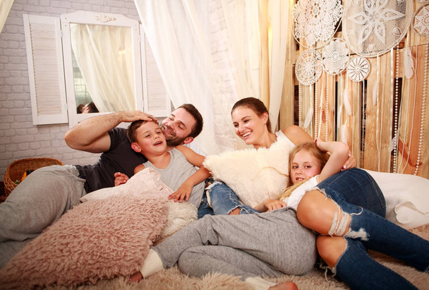Jong gezin met twee kinderen ontspannen samen thuis op bed - Foto, afbeelding
