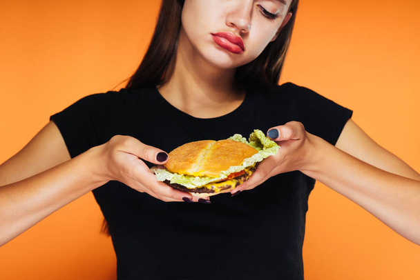 chica molesta sosteniendo una hamburguesa sobre un fondo naranja
 - Foto, imagen