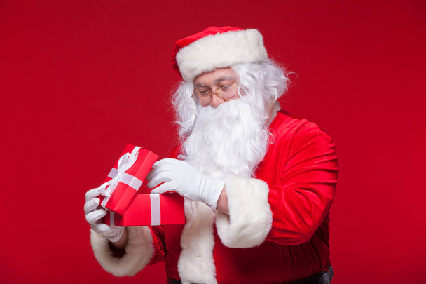 Christmas. Photo Santa Claus giving xmas present and looking at camera, on a red background - Foto, Imagem