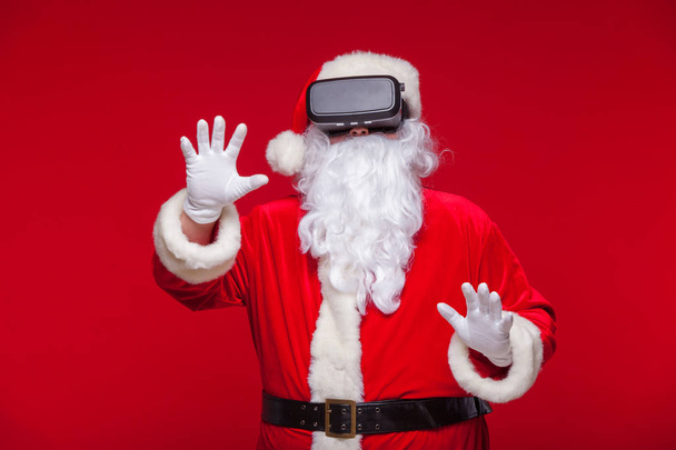 Santa Claus wearing virtual reality goggles, on a red background. Christmas - Фото, зображення