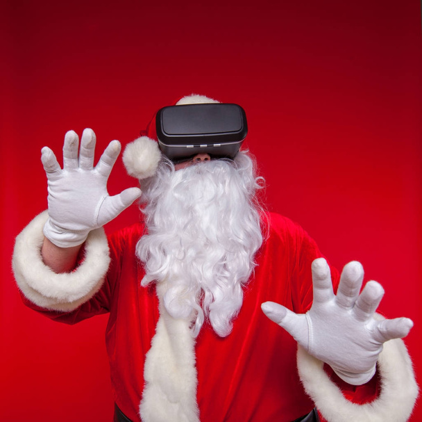 Santa Claus wearing virtual reality goggles, on a red background. Christmas - Photo, image