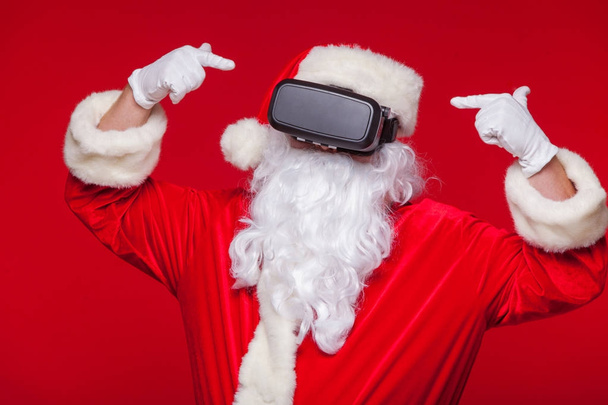 Santa Claus wearing virtual reality goggles, on a red background. Christmas - Foto, immagini