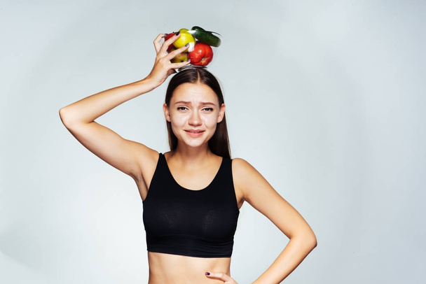 girl in sports uniform holds a bowl of vegetables over her head with vegetables - Foto, Imagem