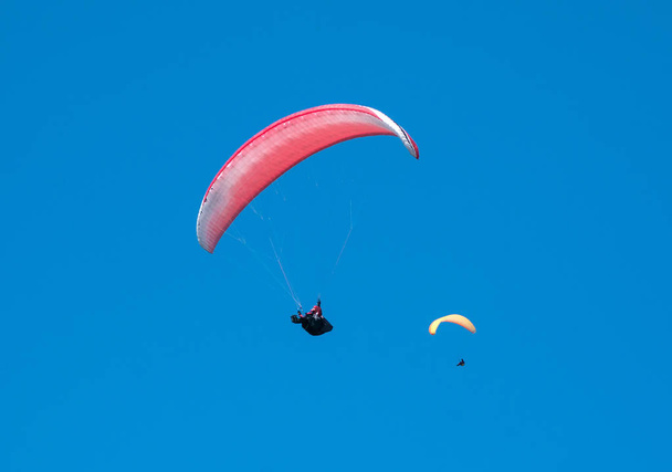 Kaksi varjoliijaa lentää taivaalla aurinkoisena päivänä.
.  - Valokuva, kuva