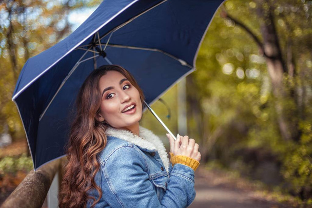 Молода красива жінка йде вздовж осіннього парку з парасолькою в руках. Осінній портрет молодої щасливої жінки. А
 - Фото, зображення