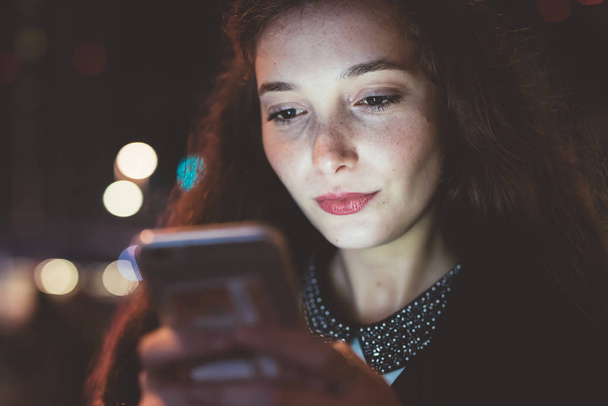 πορτρέτο νεαρή γυναίκα υπαίθρια νύχτα της πόλης χρησιμοποιώντας έξυπνο τηλέφωνο, πρόσωπο φωτίζεται από screenlight - κοινωνικό δίκτυο, internet, έννοια της τεχνολογίας - Φωτογραφία, εικόνα