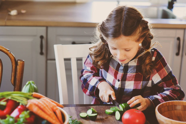 child girl helps mom to cook and cut fresh vegetables for salad with knife. Kids learning house work on farm on summer vacations - Foto, imagen