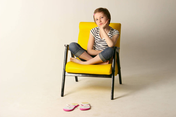 Studio πυροβολισμό από ένα νεαρό κορίτσι που κάθεται σε καρέκλα κίτρινο. - Φωτογραφία, εικόνα