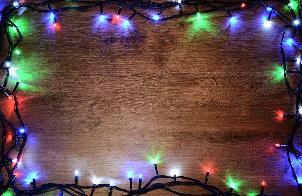 New-year electric garland on a wooden background. Bright bulbs on a wooden table and Christmas tree. - Photo, Image