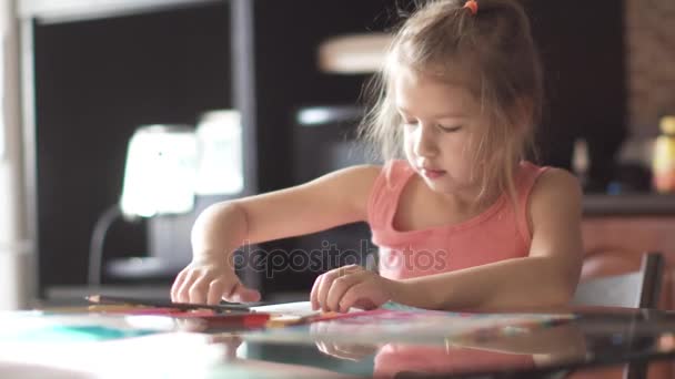 παιδί 6 ετών εφιστά σπίτια που κάθεται σε ένα τραπέζι. μικρό κορίτσι στον ήλιο το πρωί - Πλάνα, βίντεο