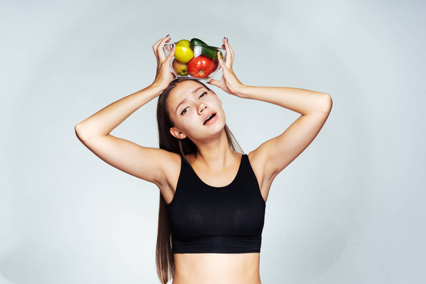 frustrated girl holding a bowl over the head with vegetables - Φωτογραφία, εικόνα