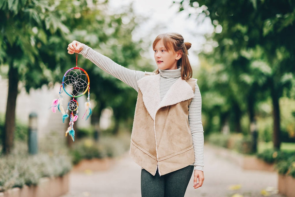Portrait extérieur d'adorable jeune fille préadolescente, tenant attrape-rêves coloré, portant un col roulé à rayures et une veste en cuir
 - Photo, image