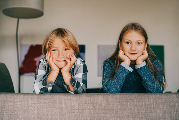 Interior portrait of two funny kids resting on the couch, looking straight at the camera - Фото, изображение