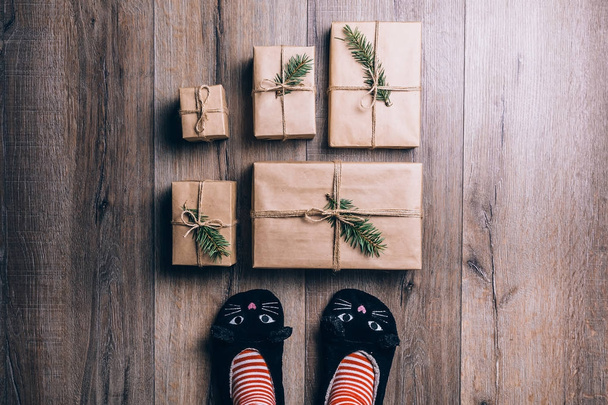 Πέλματα με ζεστό χειμώνα κάλτσες και παντόφλες γάτα που στέκεται μπροστά από τα δώρα Χριστουγέννων. το Top view. - Φωτογραφία, εικόνα